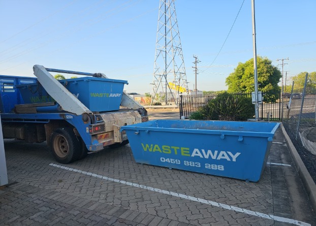 Branded NT Waste Away skip bin beside a blue delivery truck